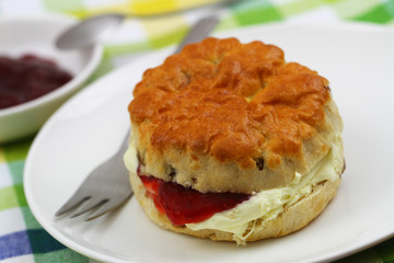 Freshly baked English scone with traditional clotted cream and strawberry jam on white plate
