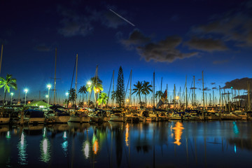 Naklejka premium Sailing boats and yachts docked at the Ala Wai Harbor, the largest yacht harbor of Hawaii, reflecting in the sea. Honolulu harbor by night, Oahu, Hawaii.