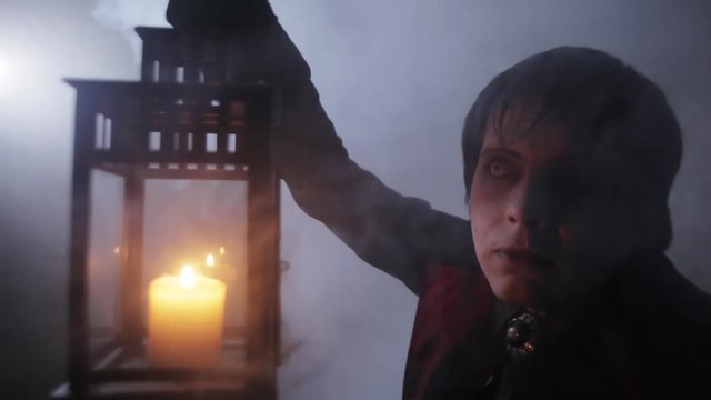 A vampire with a lamp in his hands in the mist of the night (scary man dressed in Halloween costume) 