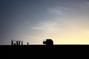 Fototapeta premium A pack of adventurers salute from the top of a grand sand dune while enjoying a beautiful summer sunset in Dakhla Oasis, Egypt.