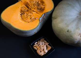 pumpkin seeds in ceramic bowl on black background with blue Nelson pumpkin sliced in half