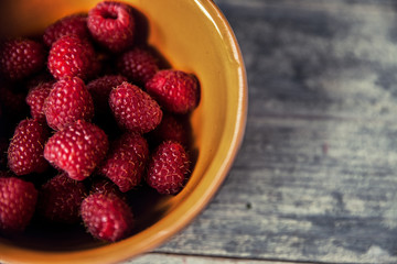 Ripe sweet raspberries in bowl on wooden table. Close up, top vi