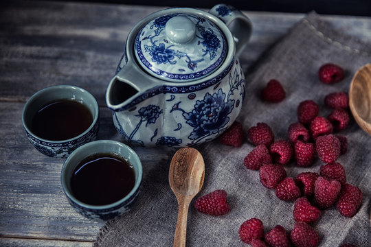 Ripe sweet raspberries in spoons on wooden table with tea pot. C