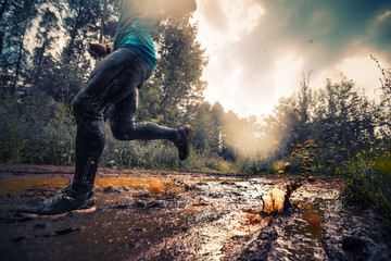 Trail running athlete moving through the dirty puddle in the rural road