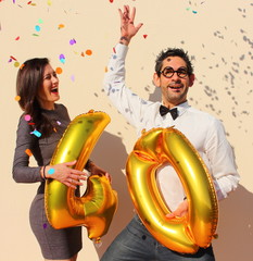Cheerful couple celebrates a forty years birthday with big golden balloons and colorful little pieces of paper in the air.