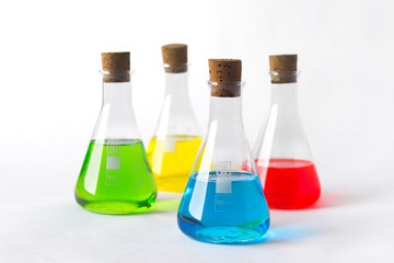 Four laboratory flasks with cork plugs and colorful liquids