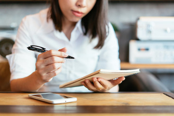 Young woman using smartphone with a coffee cup and notebook.