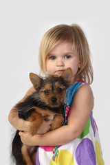 Little girl with small dog in hands on gray background