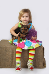 Little girl is sitting with small dog under arm on gray background © jelenaaloskina