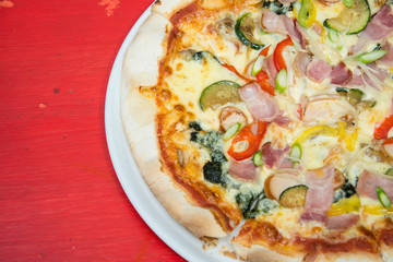 Hot pizza slice with melting cheese on red wooden table. 