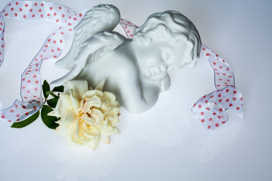 Engelchen liegend mit Herzchen- Geschenkband und weißer Rose