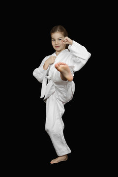 Karate practicing - little girl in sport white kimono with brave face beats foot on black background