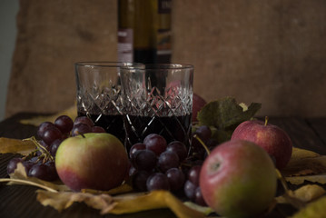 Two glasses with wine, apples and grapes on wooden surface