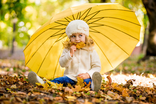 Beautiful little girl in yellow with umbrella in park