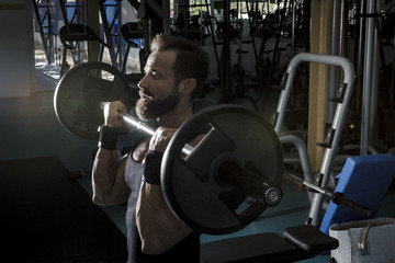 Naklejka na ściany i meble Hombre con grandes músculos levantando peso mientras entrena en el gimnasio. Ponerse en forma.