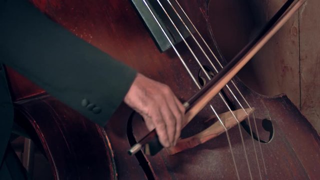 Bassist playing / Contrabass Player / Orchestra Musician. Bassist playing old dusty contrabass at a classical music concert. Bass and bow close-up.