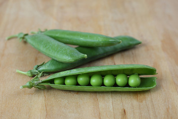 Pods of green peas on wooden cutting board close up