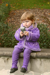 Little girl tries to use camera for self picture with a concentrated expression on her face in autumn park outdoor