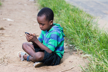 child sitting on the ground with a mobile phone in hand.