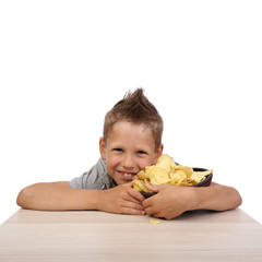 Happy teenage boy sits at the table embracing bowl with potato chips isolated on white background in square