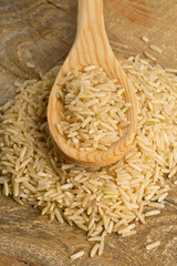 Natural brown uncooked rice in wooden spoon on wood table