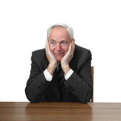 Astonished senior man sits at table isolated on white background