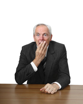 Shocked man sits at table covering her mouth by hand isolated on white background