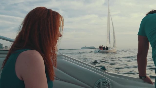Red hair girl sitting in motor boat with man. Summer evening. Entertainment. Romantic