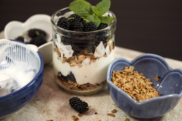Healthy snack in glass jar preparation. Yogurt berries granola and mint. Dessert in layers of fruts mulberries cream and granola.Selective focus.
