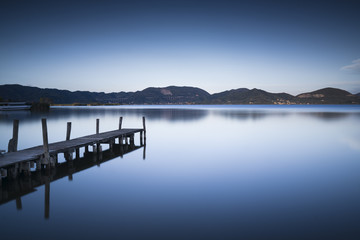 Fototapeta na wymiar Wooden pier or jetty on a blue lake sunset and sky reflection on