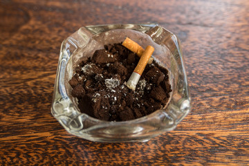 Cigarette butts with ash in ashtray on wooden table