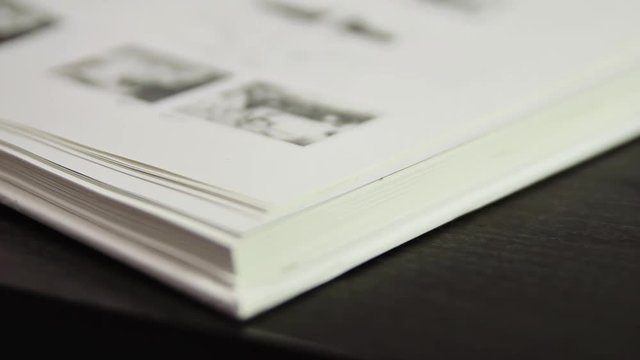 Slow flipping book pages. The book is illustrated with black-and-white photos. Shallow depth-of-field.