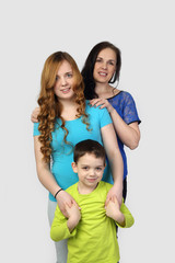 Woman, girl and little boy stand in sequence one behind other on gray background  - incomplete family portrait