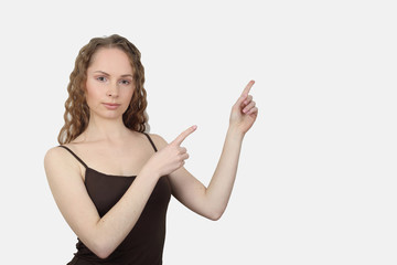 Serious young woman in shirt shows direction with bare arms pointing fingers on gray background...