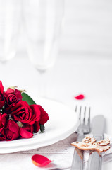 Festive table setting with beige roses, wine glasses, napkins and cutlery,