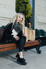 Fototapeta na wymiar Beautiful tired woman after shopping on bench. Beautiful Portrait of sensual young model wearing a coat and grey scarf. With glamour red lips make-up, eye arrow makeup, purity skin