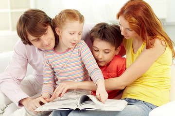 Family of four reading book together at home