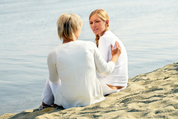 Mother with daughter sitting near the water and talking