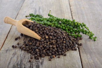 fresh green peppercorns and dry black pepper on wooden table