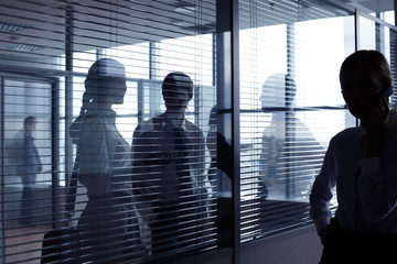 Unrecognizable business people communicating behind glass wall with blinds