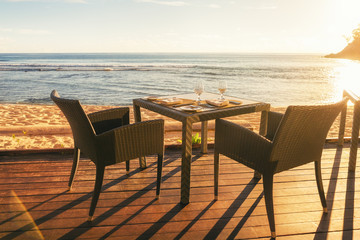 Dining table and two chairs on decking by sea side at evening su