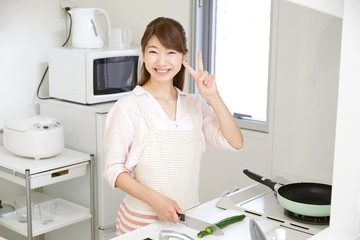 キッチンに立つ女性　ピースサイン