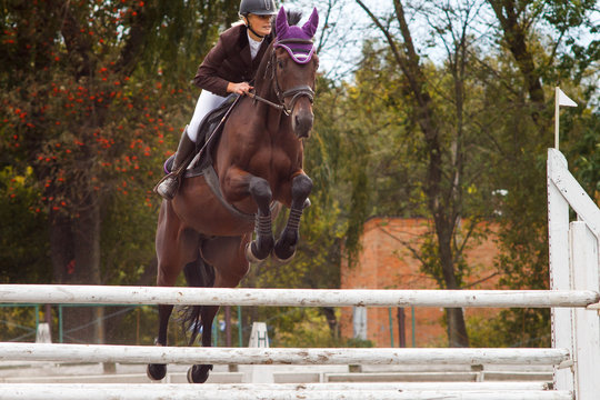 Young rider girl jumping over barier on her course
