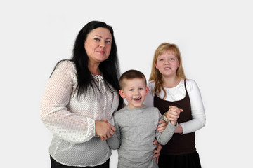 Brunette adult woman and teenage blonde girl hold smiling little toothless boy hands on gray background - mother, son and daughter - family relations and love concept