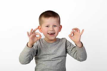 Little toothless boy with wide happy smile on face shows okey sign on gray background