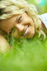 Beautiful woman lying on grass and smiling at camera