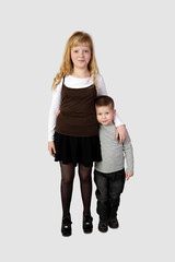 Little boy and older girl stand embraced in full height on gray background - love and friendship concept - sister and brother