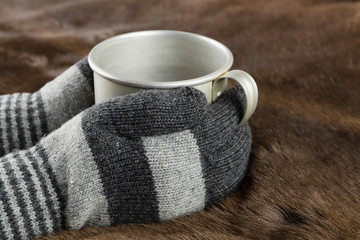 Hands in knitted gloves keep mug