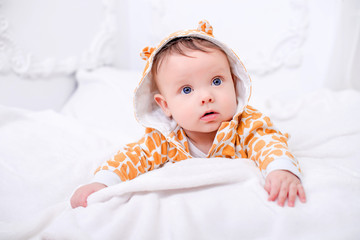 A cute little baby is looking into the camera on the white wall.