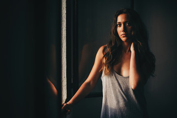 Beautiful woman in grey with hand on neck at window